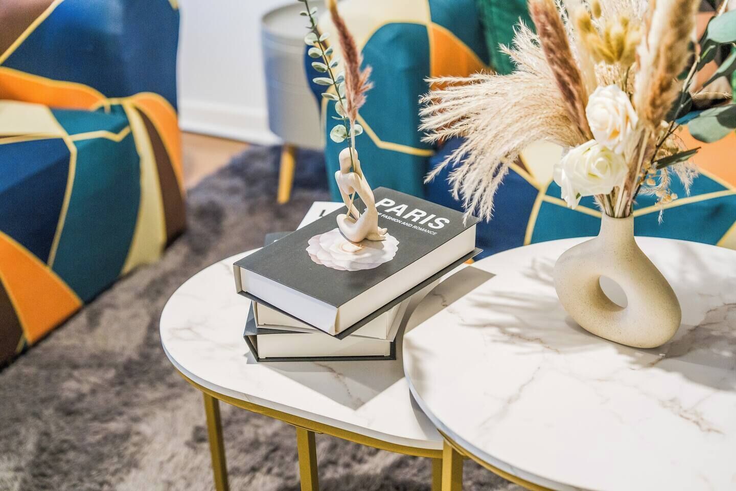 A stack of books on a white marble table with a vase of dried flowers.