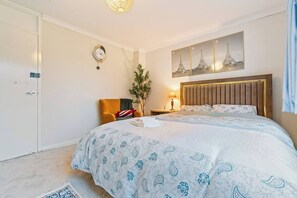 A hotel room with a bed, a nightstand, a lamp, a clock, and a wall-mounted artwork.