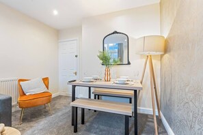 A dining area with a table set for two, a chair, a floor lamp, and a mirror on the wall. - #97 Historic Grade II Cottage Near NEC (Coleshill)
