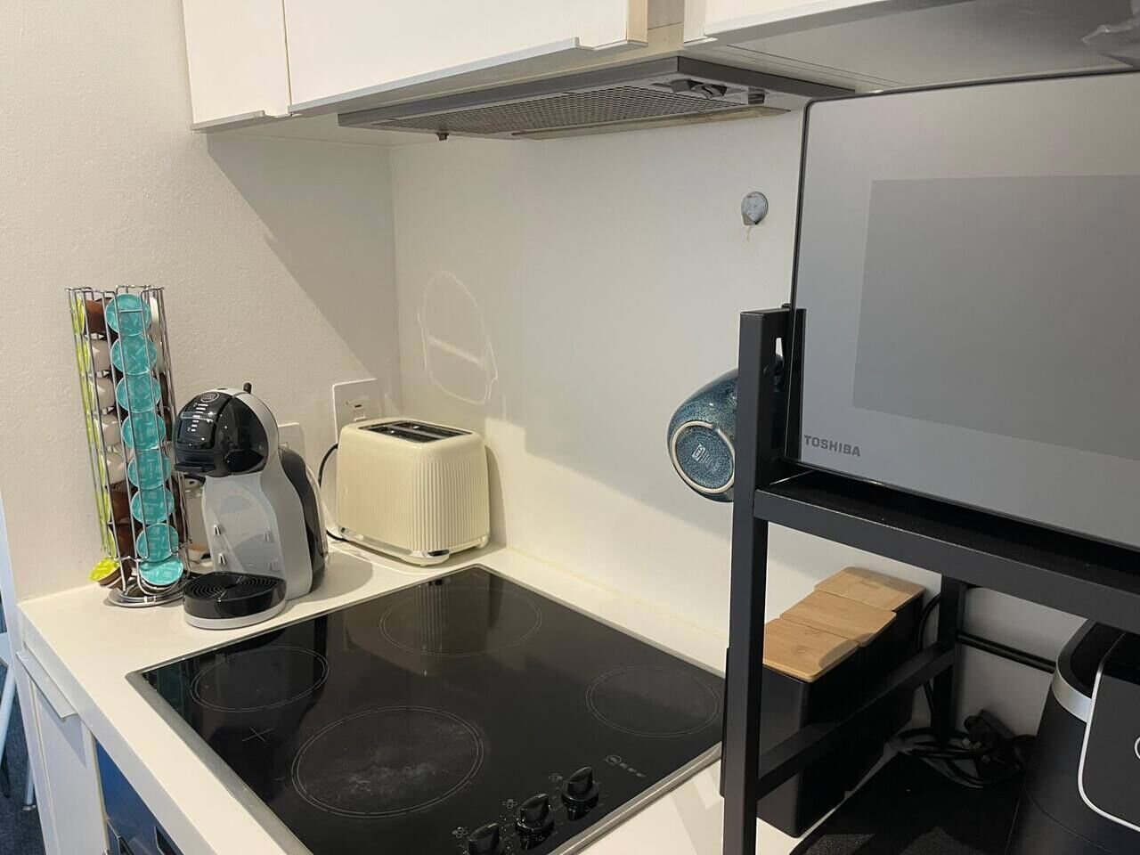 Une cuisine compacte équipée d’une plaque de cuisson à induction noire, d’un grille-pain et d’un réfrigérateur.