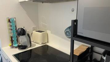 Una cocina compacta con una placa de inducción negra, un tostador y un refrigerador.