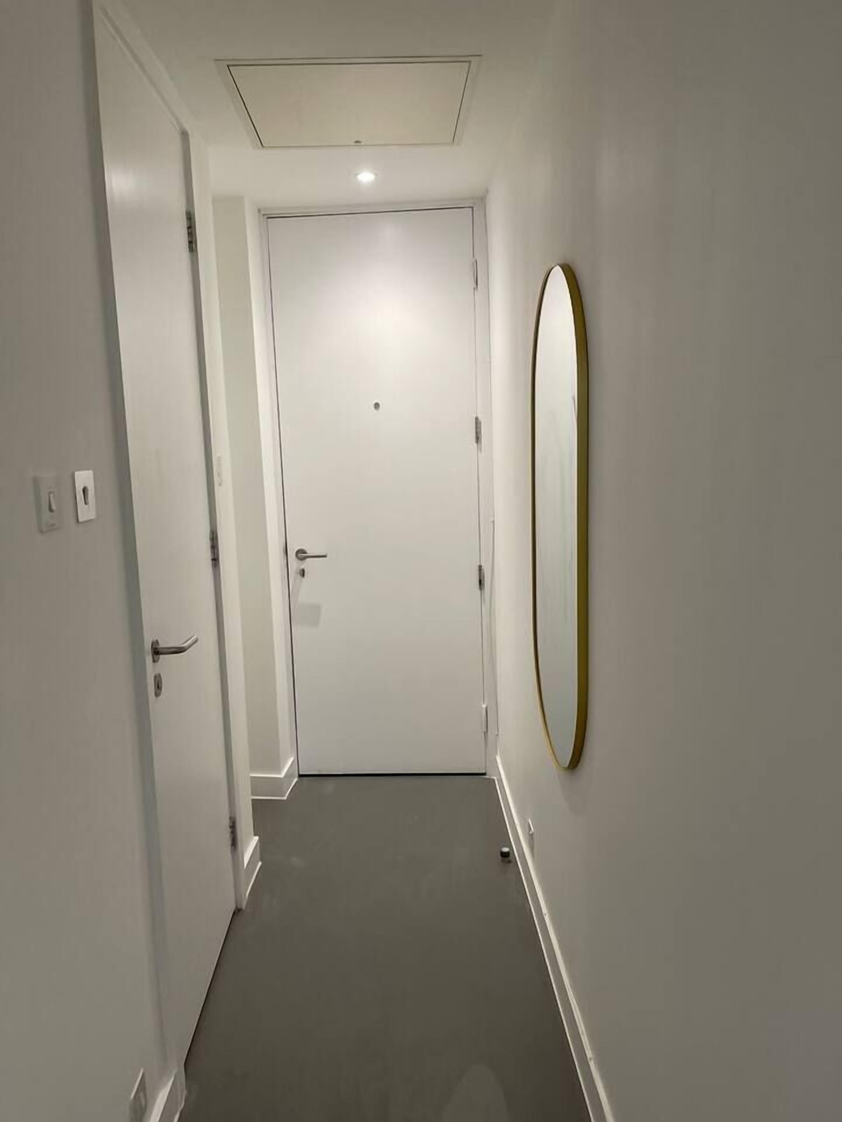 A narrow hallway with a closed door at the end, a light switch, and a wall-mounted oval mirror.