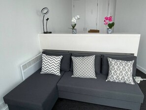 A modern room with a grey sectional sofa, three patterned pillows, a small table with a lamp, and two potted plants. - #96 World Famous The Rotunda 17th Floor (West Midlands)