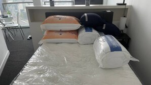 Ein Hotelzimmer mit einem mit Schutzfolie bezogenen Bett, Kissen und einem Nachttisch mit Lampe.