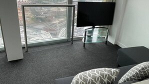 Ein modernes Hotelzimmer mit einem großen Fenster, einem Flachbildfernseher, einem Glastisch und einer Couch mit gemusterten Kissen.