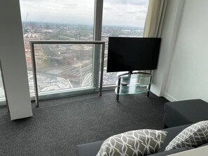 A modern hotel room with a large window, a flat-screen TV, a glass table, and a sofa with patterned cushions. - #96 World Famous The Rotunda 17th Floor (West Midlands)