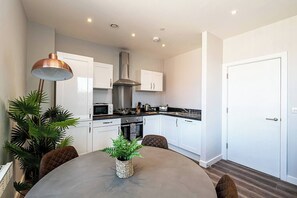 A modern kitchen with white cabinets, a stainless steel range hood, and a dining table with chairs. - #95 Crosby Gardens Apartment 2 beds & 1 bath (Waterloo)