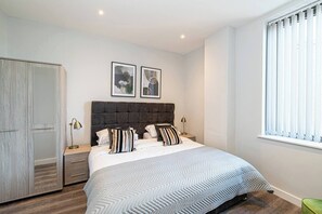 A bedroom with a bed, bedside tables, a wardrobe, and a window with curtains. - #95 Crosby Gardens Apartment 2 beds & 1 bath (Waterloo)