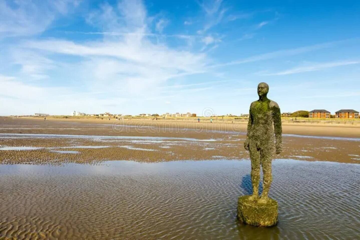 A statue on a rock in a sandy area with buildings in the background.