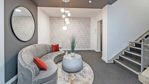 Ein modernes Interieur mit einem gebogenen grauen Sofa, einem runden Couchtisch und einer Treppe.
