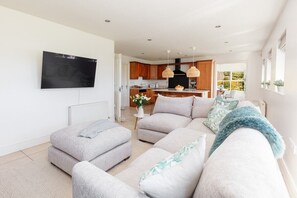 Ein modernes Wohnzimmer mit einem Ecksofa, einem flachbildfernseher an der Wand und einer Küche im Hintergrund.