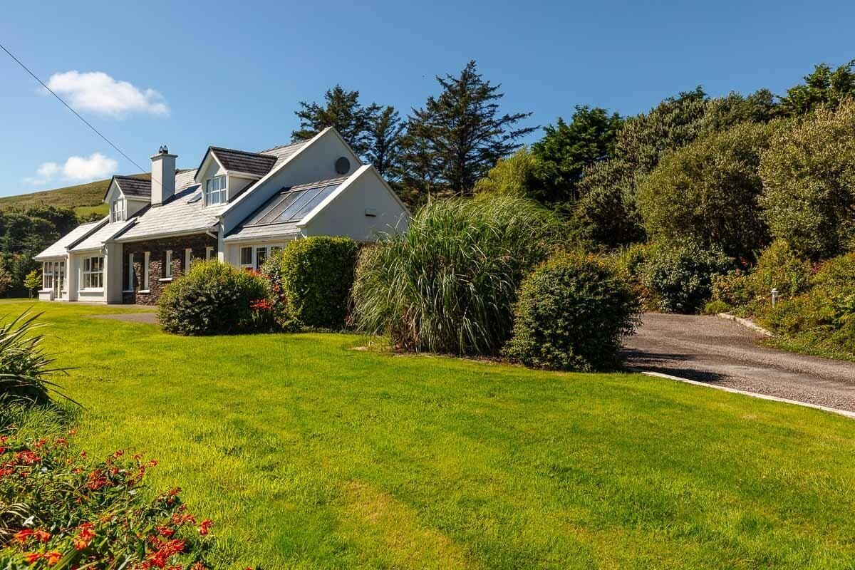 A two-story house with a sloped roof, a driveway, and a well-maintained lawn with shrubs and flowers.