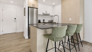 Uma cozinha moderna com geladeira de aço inoxidável, forno embutido, pia e área de bar com banquetas estofadas em verde.