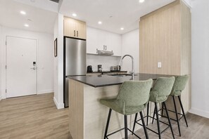 A modern kitchen with a stainless steel refrigerator, a built-in oven, a sink, and a bar area with green upholstered bar stools. - The Downtown Sugar Shack | Rooftop Pool | Sleeps 8 (Québec)