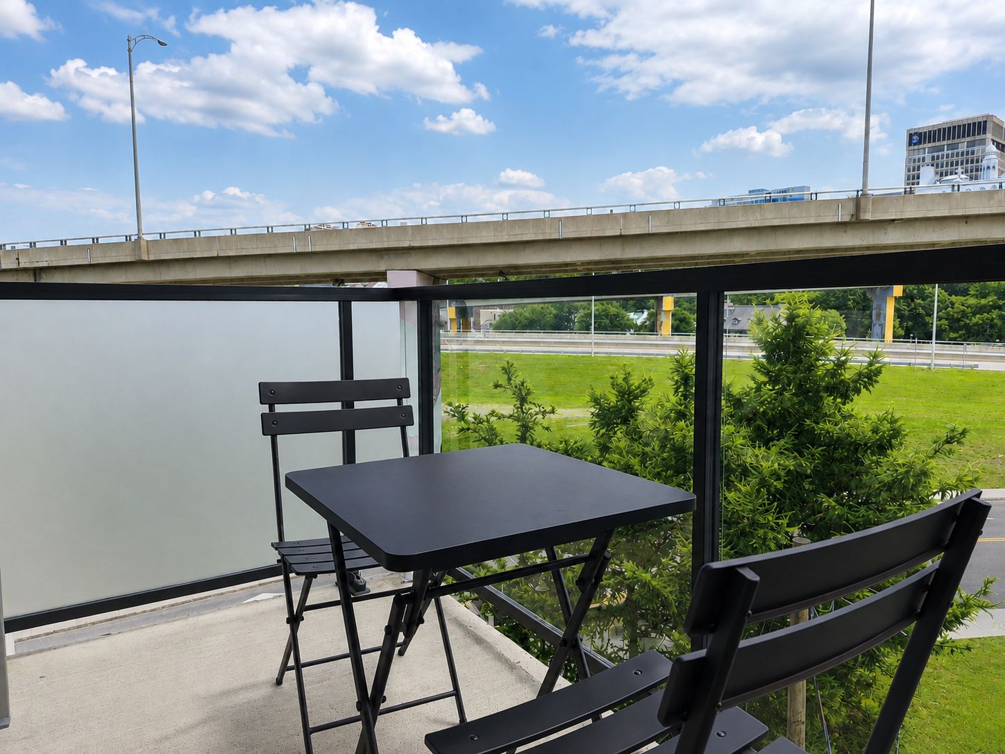 A balcony with a table and two chairs, overlooking a highway and greenery.