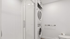 Um banheiro moderno com box de vidro, máquina de lavar roupa dupla e vaso sanitário.