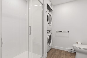 A modern bathroom with a glass shower enclosure, a double washing machine, and a toilet. - The Downtown Sugar Shack | Rooftop Pool | Sleeps 8 (Québec)