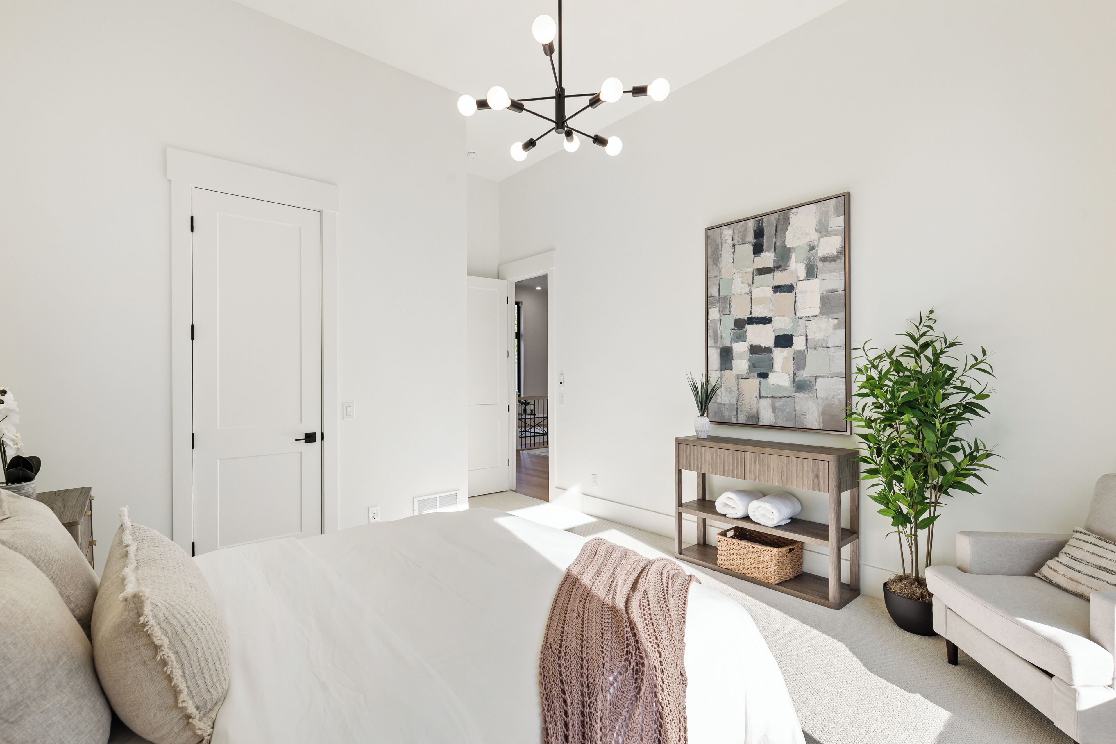 Un dormitorio moderno con una cama grande, una consola de madera, una planta en maceta y un cuadro abstracto de gran tamaño en la pared.