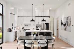 Una cocina moderna con armarios blancos, una isla central con asientos, iluminación colgante y un cuadro abstracto grande en la pared.