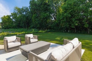 An outdoor seating area with a sofa and chairs, a table, and a lawn. - Modern House in Chaska (Chaska)