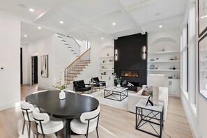 A modern living room with a fireplace, a dining area with a round table and chairs, and a staircase with wooden railings. - Modern House in Chaska (Chaska)