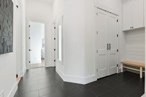 A hallway with a dark floor, white walls, and a bench. There are two doors with black handles and a white wall-mounted shelf. - Modern House in Chaska (Chaska)
