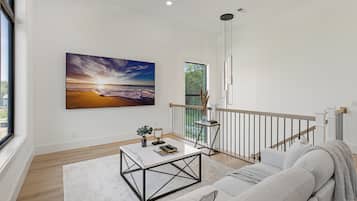A modern living room with a large painting of a beach scene, a white sofa, a coffee table, and a view of a balcony.