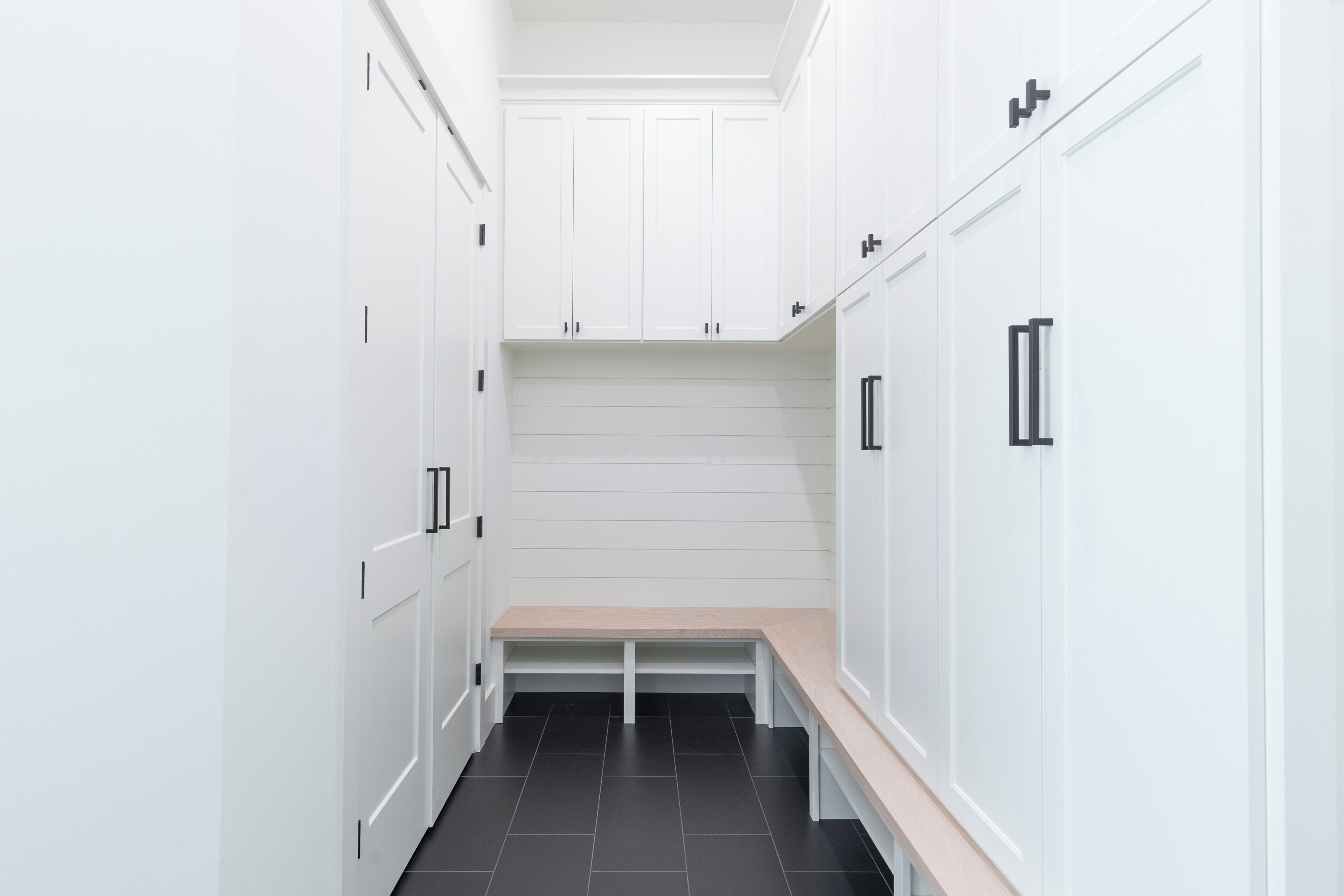 A narrow hallway with white cabinetry and a bench.