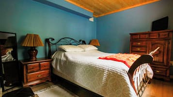 A bedroom with a bed, two bedside tables, a dresser, a mirror, and a television.