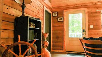 A wooden cabin interior with a rocking chair, a wooden cabinet with books, and a door with a window.