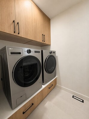 A compact laundry room with two LG washing machines, wooden cabinets, and a white tiled floor. - Haven on 54th | Modern Luxury Retreat | 3BR 2.5BA Sleeps 6 (Calgary)