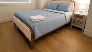 Een slaapkamer met een bed, nachtkastje en een raam met zonwering.