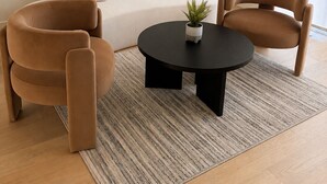 Een moderne woonkamer met een bank, twee fauteuils, een salontafel en een potplant.