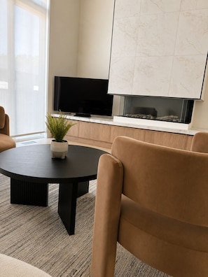Una sala moderna con una mesa redonda, televisor de pantalla plana, chimenea y sofá.