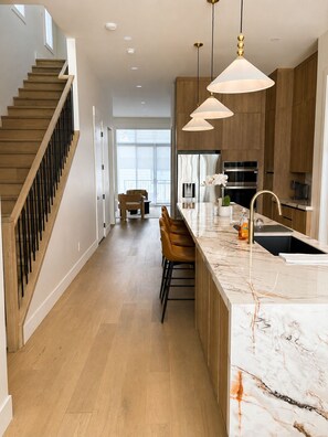 A modern kitchen with a marble countertop, wooden cabinets, and pendant lighting. - Haven on 54th | Modern Luxury Retreat | 3BR 2.5BA Sleeps 6 (Calgary)