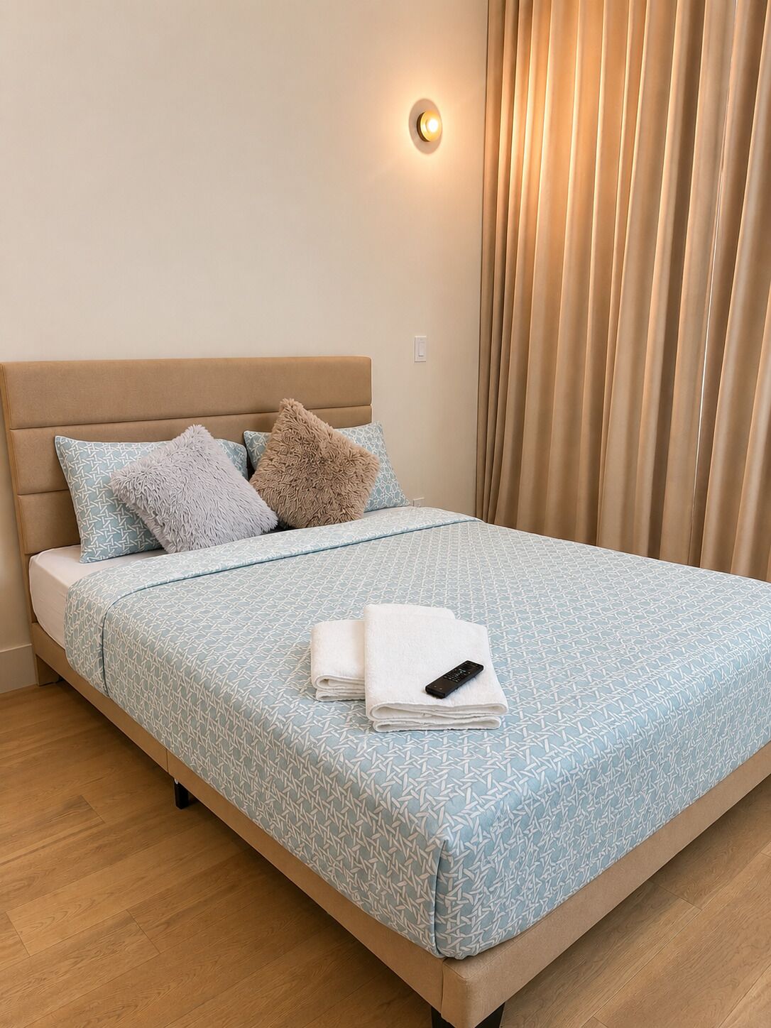 Cama bem arrumada com colcha estampada, dois travesseiros e um controle remoto sobre uma toalha dobrada.