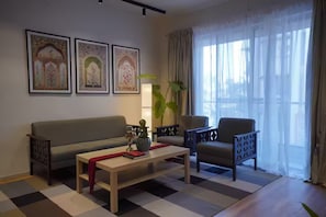 A living room with a sofa, armchair, coffee table, and a large window with curtains.