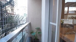 A narrow balcony with a metal railing, a potted plant, and a sliding glass door leading to an interior space.