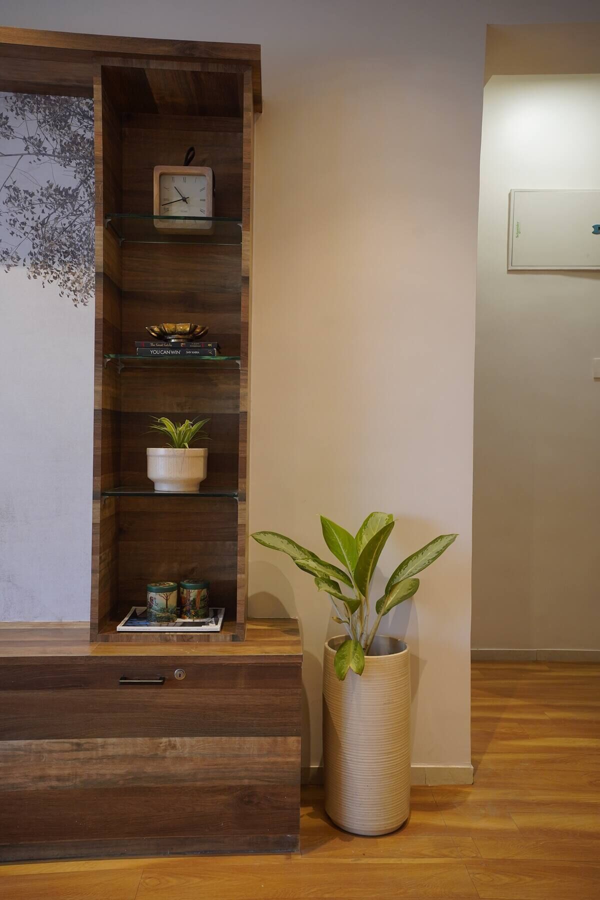 A wooden cabinet with a clock, shelves with books, and a potted plant.