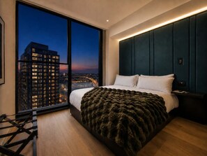 A modern bedroom with a large window, a bed with a dark blanket, and a city view at dusk. - Elite E11EVEN Studio with Rooftop Pool & Resort Gym (Miami)