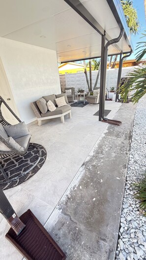 Un área de estar al aire libre con mobiliario de mimbre y piso de concreto.