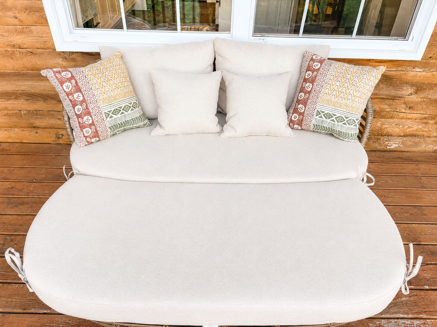 Uma cama com colchão e almofadas bege, apoiada em uma parede de madeira com uma janela acima.