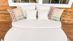 Uma cama com colchão e almofadas bege, apoiada em uma parede de madeira com uma janela acima.