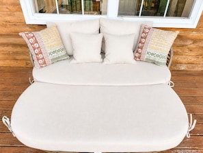 A bed with a beige mattress and pillows, set against a wooden wall with a window above.