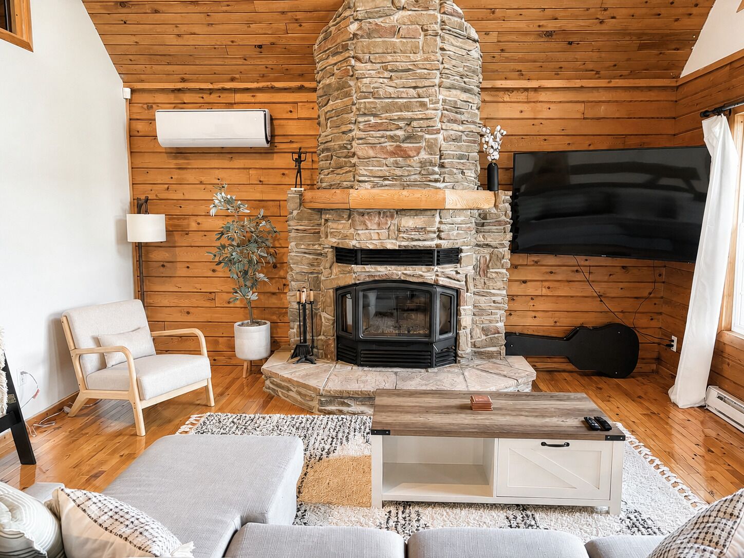 Un salon chaleureux avec une cheminée en pierre, des murs en bois, un téléviseur à écran plat et un coin salon confortable.