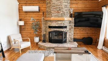 Un salon chaleureux avec une cheminée en pierre, des murs en bois, un téléviseur à écran plat et un coin salon confortable.