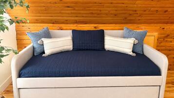 A sofa bed with a dark blue cover, light-colored cushions, and a wooden wall background.