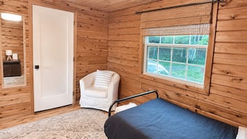 A wooden cabin room with a bed, a chair, a window, and a door.