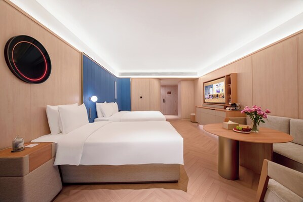 A modern hotel room with a large bed, a desk, a seating area, and a television.