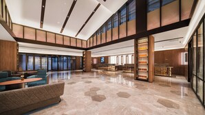 A spacious lobby with a high ceiling, a central seating area with sofas and tables, and a bar area with shelves of bottles.